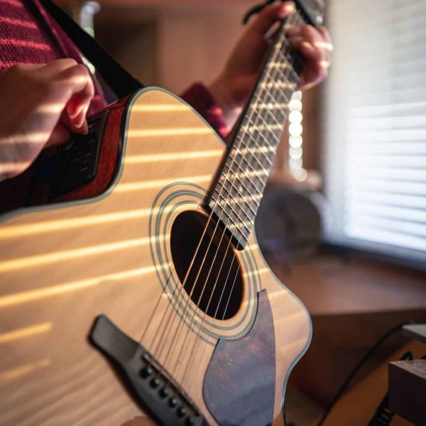 A girl with an acoustic guitar in the sunlight, through the blinds, early in the morning.